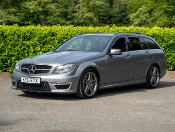 Gray Mercedes-Benz station wagon parked outdoors with greenery in the background.