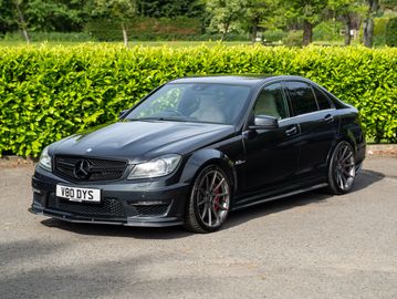 Black Mercedes-Benz sedan parked on a driveway with greenery in the background.