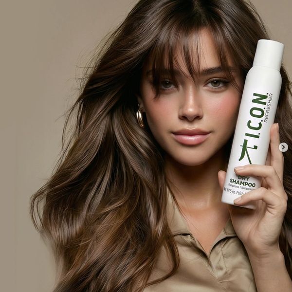 Woman with long brown hair holding a bottle of I.C.O.N. dry shampoo.