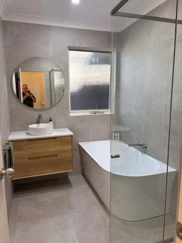 Modern bathroom with a bathtub, floating vanity, and round mirror.