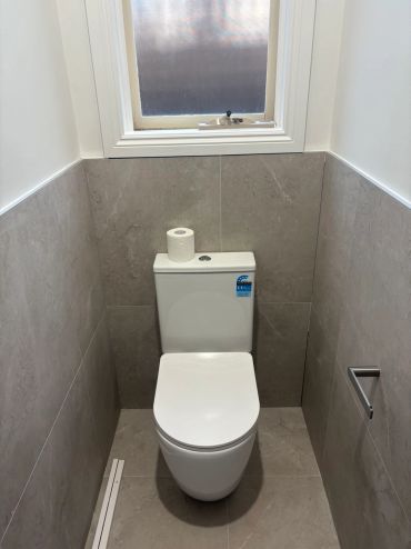 Modern toilet in a small, tiled bathroom with a window above.