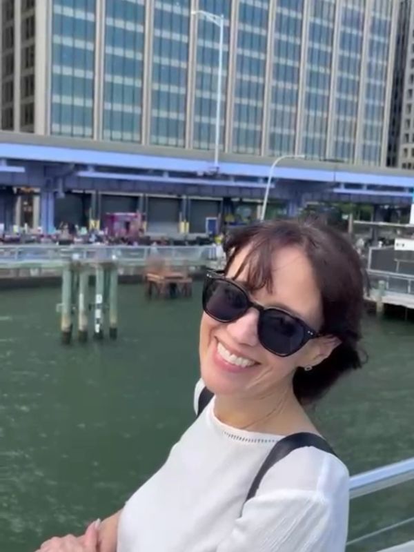Woman smiling by the waterfront, wearing sunglasses.