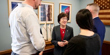 A woman in a suit talks with three people in an office.
