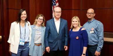 Five professionals posing together indoors with an American flag in the background.