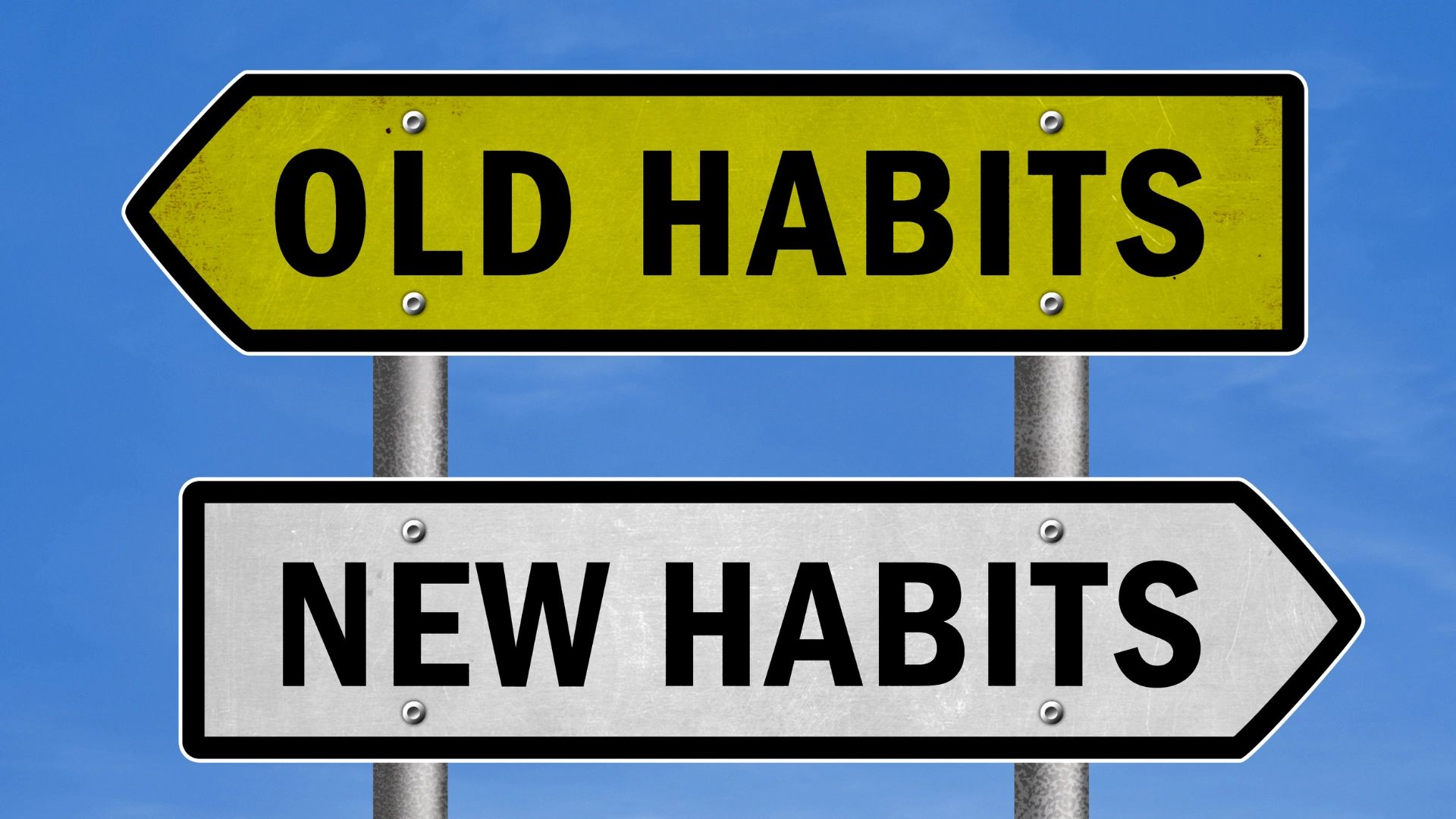 Directional signs pointing to old habits and new habits under a clear blue sky.