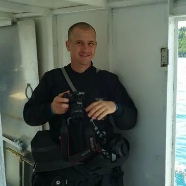 A man holding a Canon camera inside a boat near water.