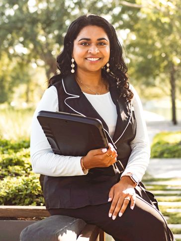 Smiling woman in professional attire holding a tablet outdoors.