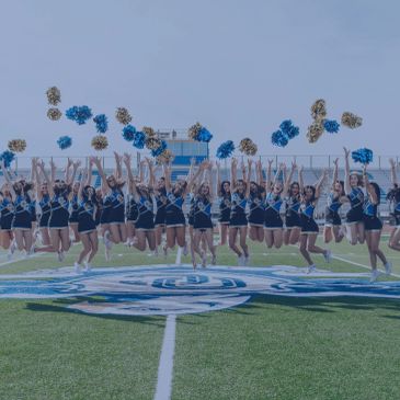Cheerleaders jumping with pom-poms on a football field.