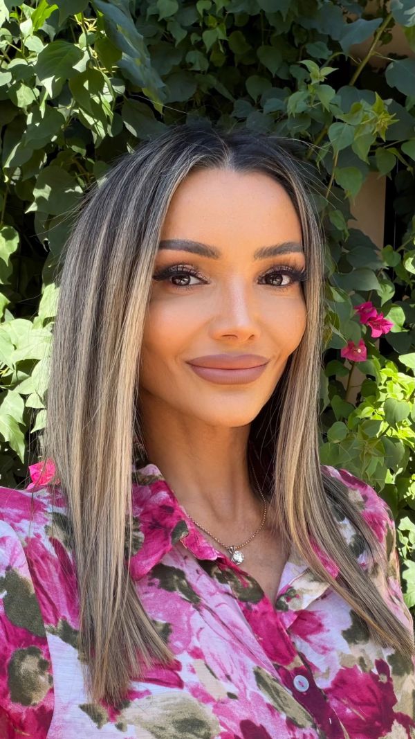 Woman with straight hair and floral shirt smiles outdoors.
