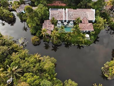 A villa with a pool surrounded by water and lush greenery.