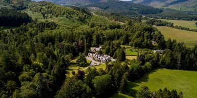 Large house surrounded by dense forest and fields.