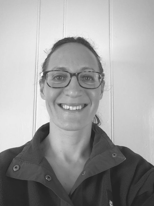 Smiling woman wearing glasses and a jacket, with hair tied back.