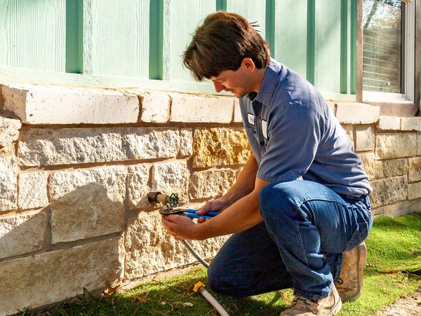 Man fixing outdoor water faucet on stone wall.
