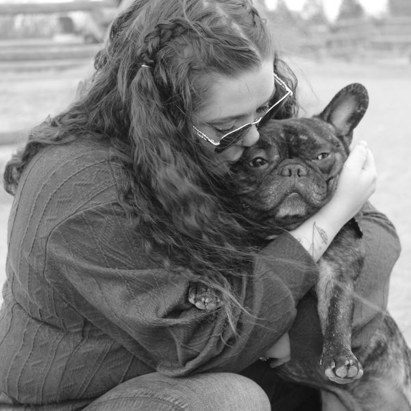 Woman with curly hair hugging a French Bulldog.