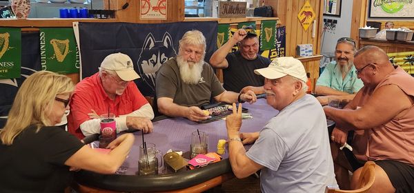 A group of seven adults playing cards around a table in a cozy room.