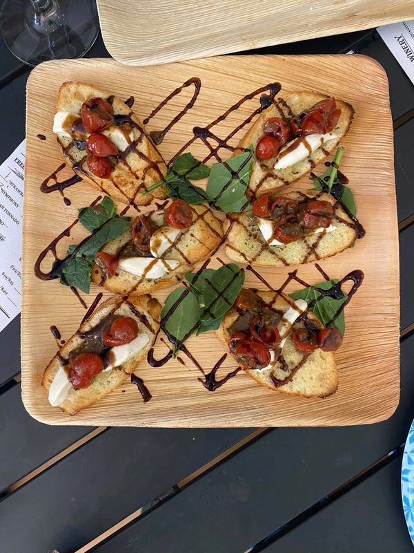 Toasted crostini with mozzarella, cherry tomatoes, greens, and balsamic glaze on a wooden platter.