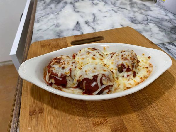Baked meatballs covered with melted cheese in a white dish.