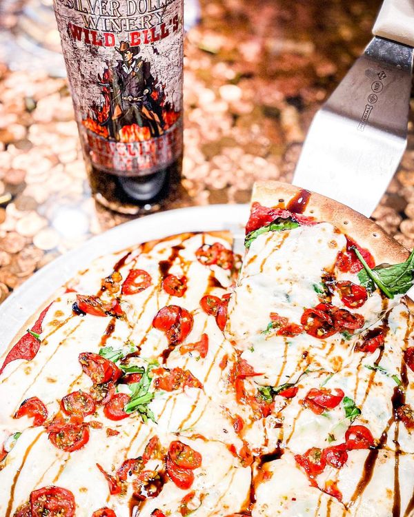 Fresh pizza with cherry tomatoes and balsamic glaze, paired with a bottle of Wild Bill's wine.
