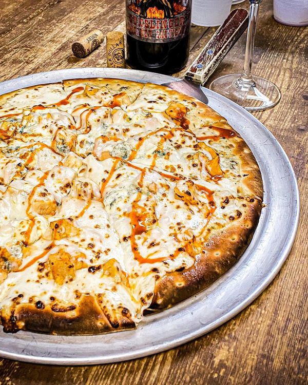 Buffalo chicken pizza with melted cheese and hot sauce on a metal tray.