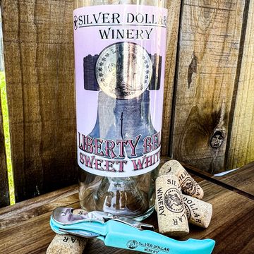 A Silver Dollar Winery Liberty Bell Sweet White wine bottle with corks and a blue wine opener.