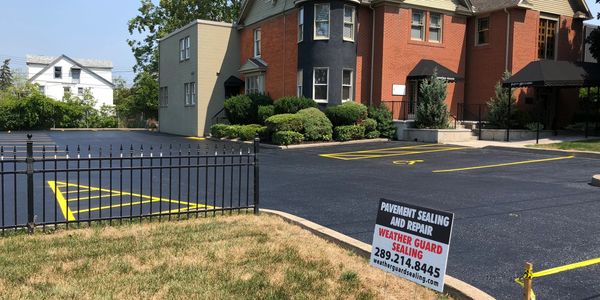Freshly sealed parking lot with bright yellow lines outside a brick building.