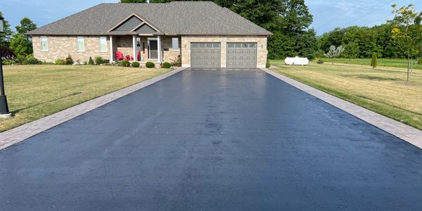 Large driveway leading to a brick house with double garage and lawn.