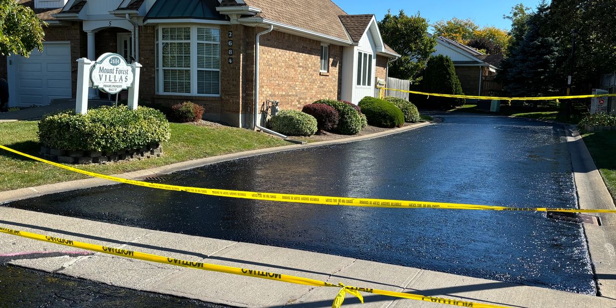 Freshly paved road section blocked off with caution tape near suburban villas.
