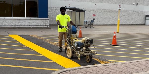 Worker painting yellow lines in a parking lot with a line marking machine.