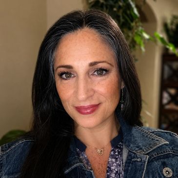 Woman smiling with long dark hair and denim jacket.