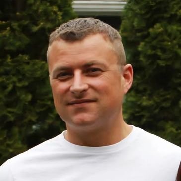 Man with short hair in a white shirt outdoors.