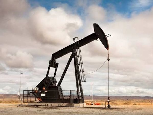 A black oil pumpjack operating in a desert under a cloudy sky.
