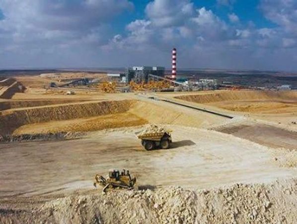 Heavy machinery operates at a large mining or construction site under a cloudy sky.