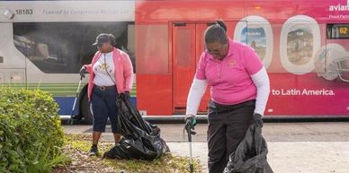 Two women cleaning outdoors with bags and grabbers.