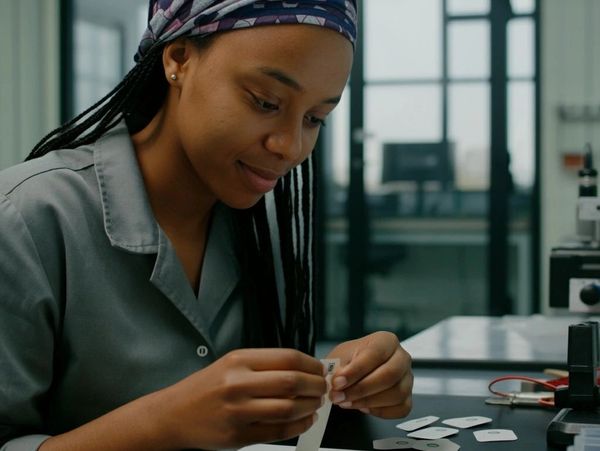 Woman in a lab coat examining slides at a laboratory table.