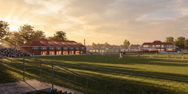 A cricket match at sunset with spectators and buildings.