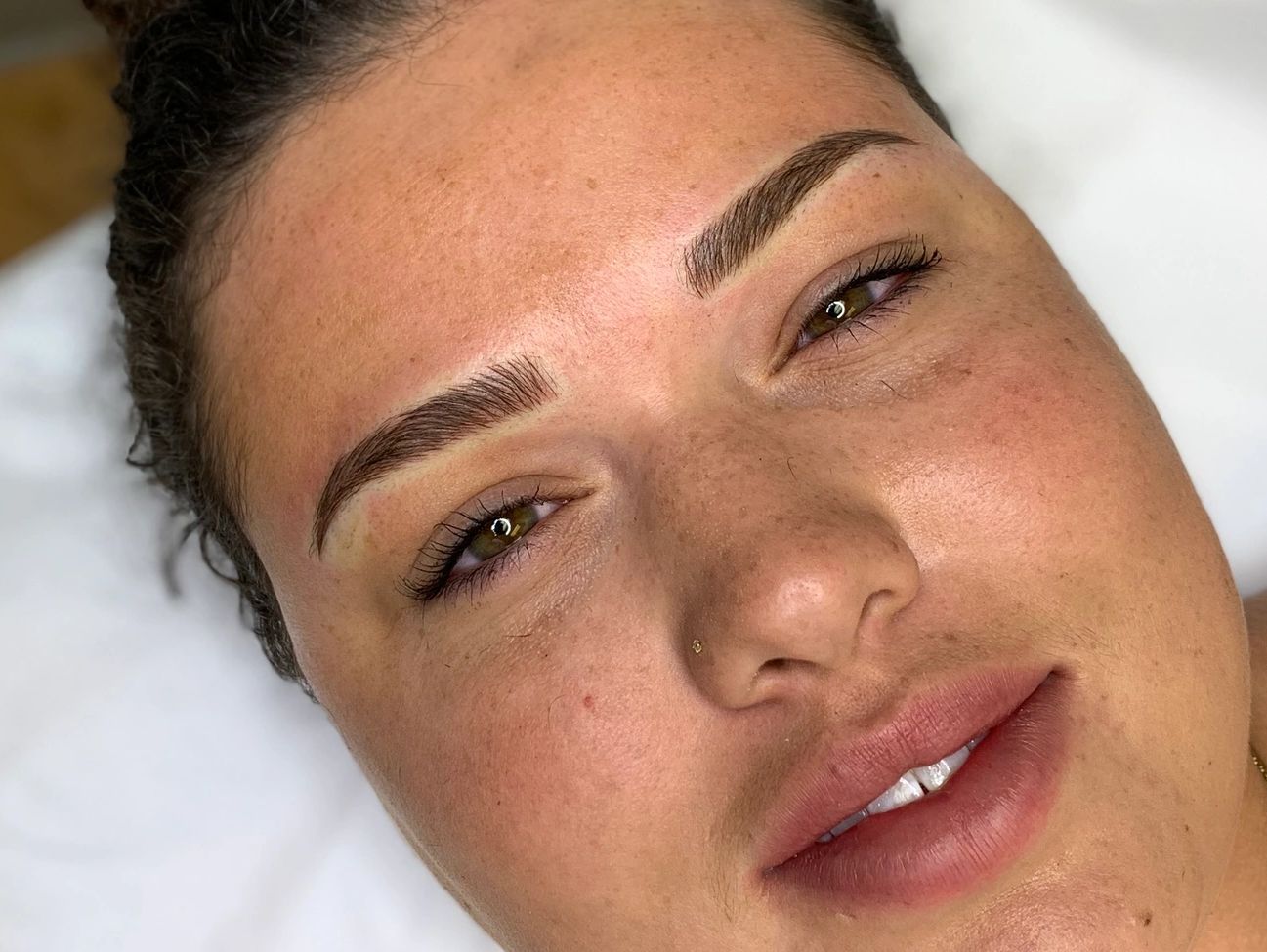 A woman with combo brows lying down on a pillow