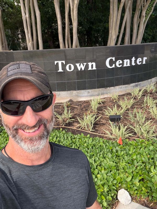 adam taylor the handyman standing in front of the town center entrance sign in the woodlands tx