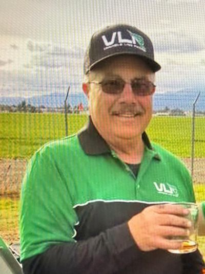 Man in green VLR shirt and cap holding a drink outdoors.