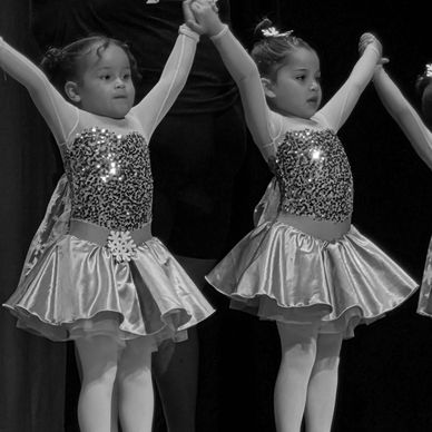 Two young girls in sparkly dance costumes on stage.