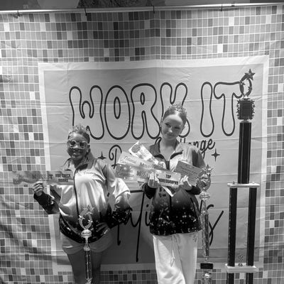 Two girls holding trophies and awards at a dance competition.