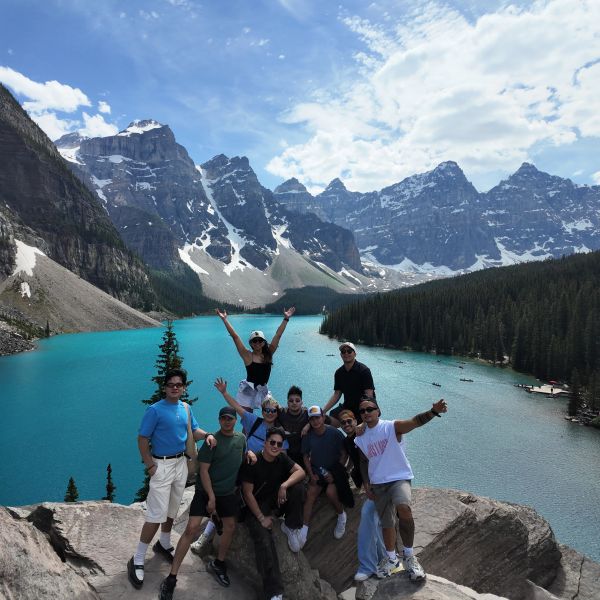 Group posing near a turquoise lake with mountainous backdrop.