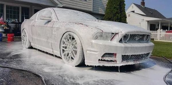 A car covered completely in thick white soap foam during washing.