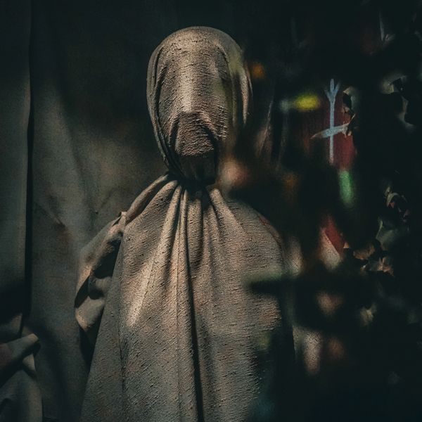 Figure covered in textured fabric, creating a mysterious silhouette.