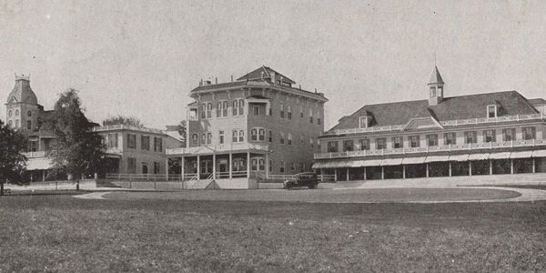 Black and white photo of early 20th-century buildings with vintage cars.