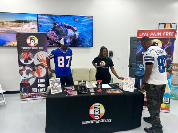 People promoting Emergency Muscle Stick for pain relief at an indoor event.