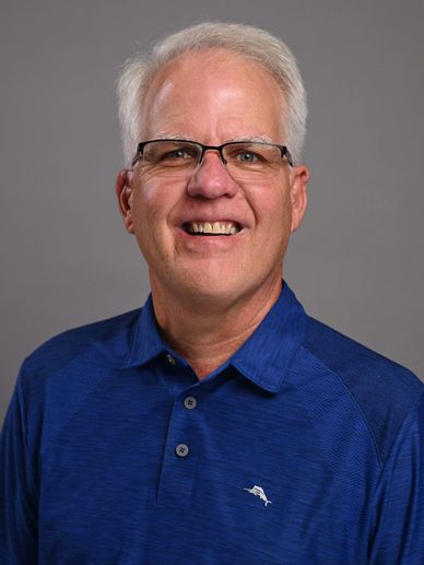 Smiling elderly man with white hair wearing glasses and a blue polo shirt.