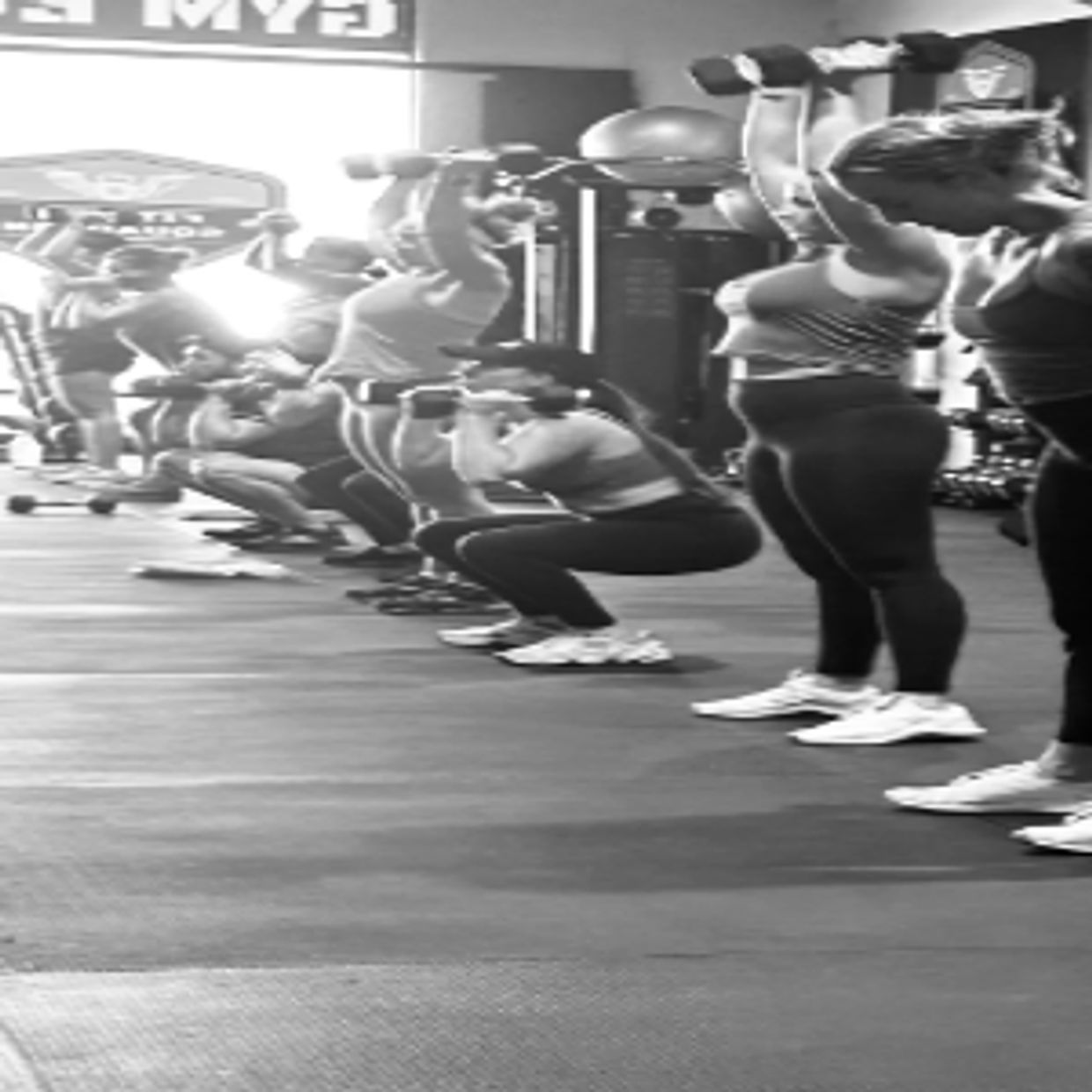 Group workout session with women lifting weights in a gym.