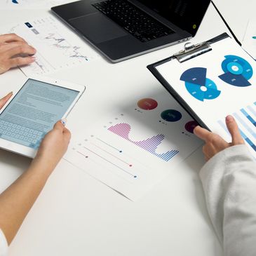 Three people analyzing charts and data on paper, tablet, and laptop (simulating analyzing a privacy report) at a white table.