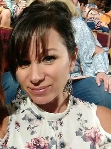Woman smiling in a floral dress at a crowded event.