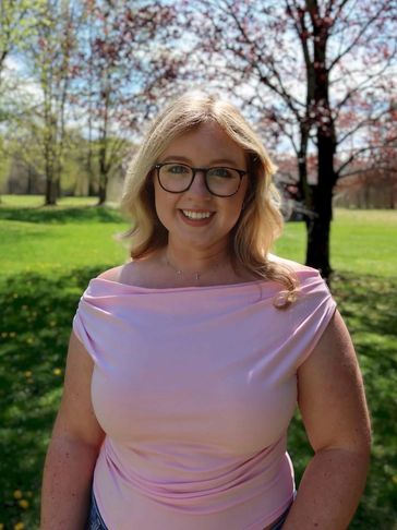Smiling woman in a pink top standing outdoors on a sunny day.